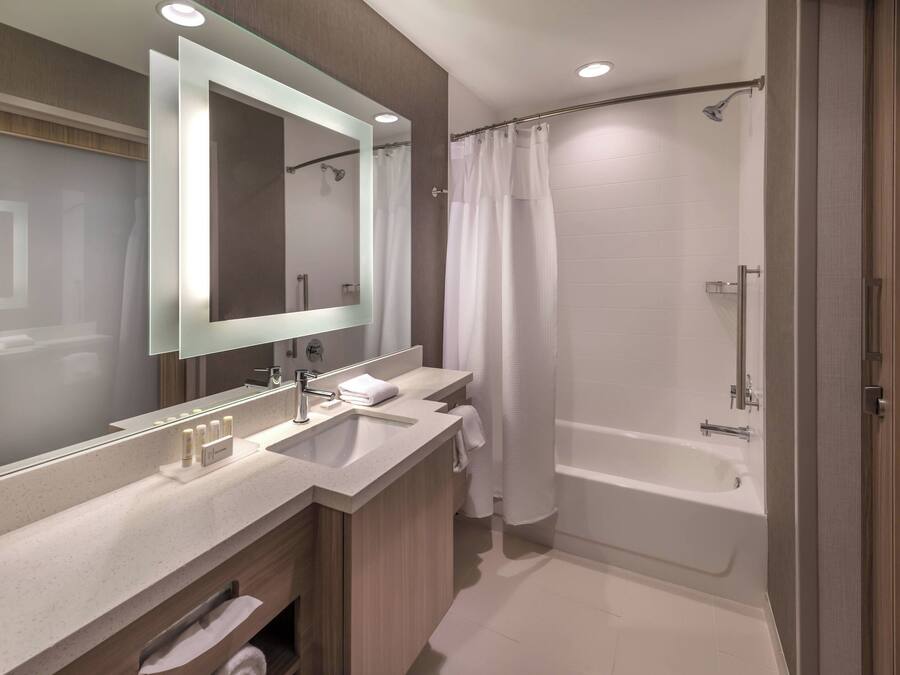 A modern bathroom with a double sink vanity, a large mirror, a bathtub, and a shower curtain.