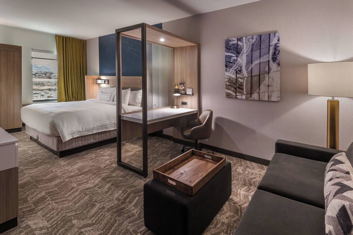 A hotel room with a bed, desk, chair, and ottoman.