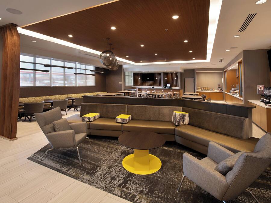 A modern hotel lobby with a large seating area, a bar, and a kitchen in the background.