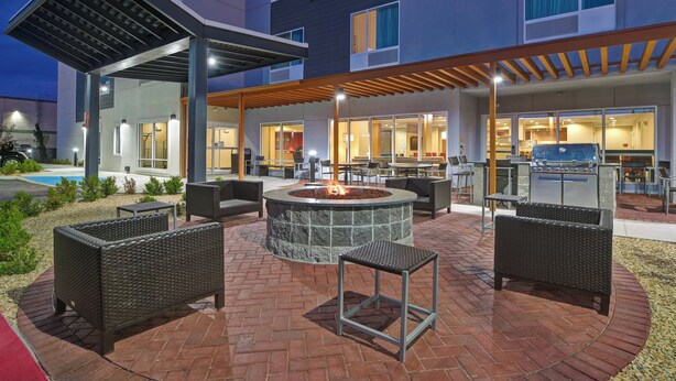 A hotel patio with outdoor seating, a fire pit, and a pool in the background.