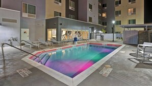 A swimming pool with a glass enclosure, surrounded by lounge chairs and a covered seating area.