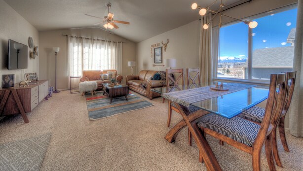 A spacious living room with a large dining table, leather sofa, and a ceiling fan. - Quiet home with a view and AC!! (Colorado Springs)