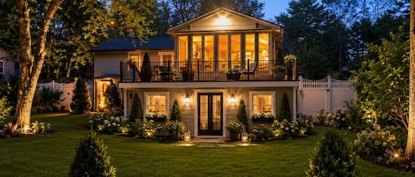 A two-story house with a balcony, surrounded by a well-maintained lawn and trees.