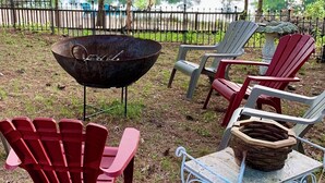 A lakeside outdoor seating area with Adirondack chairs and a metal table, surrounded by a metal fence and trees. - Waterfront Quiet Retreat, Plymouth, Pet Paradise, Private Beach, Sleeps 4 (Plymouth)