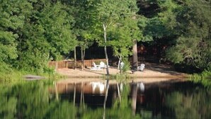 A serene lakeside setting with a wooden deck and a boat, surrounded by dense trees. - Waterfront Quiet Retreat, Plymouth, Pet Paradise, Private Beach, Sleeps 4 (Plymouth)