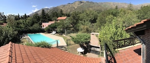 A pool area with a mountain backdrop, surrounded by trees and a red-roofed building. - Chalet Paseo del Zorzal (Merlo)