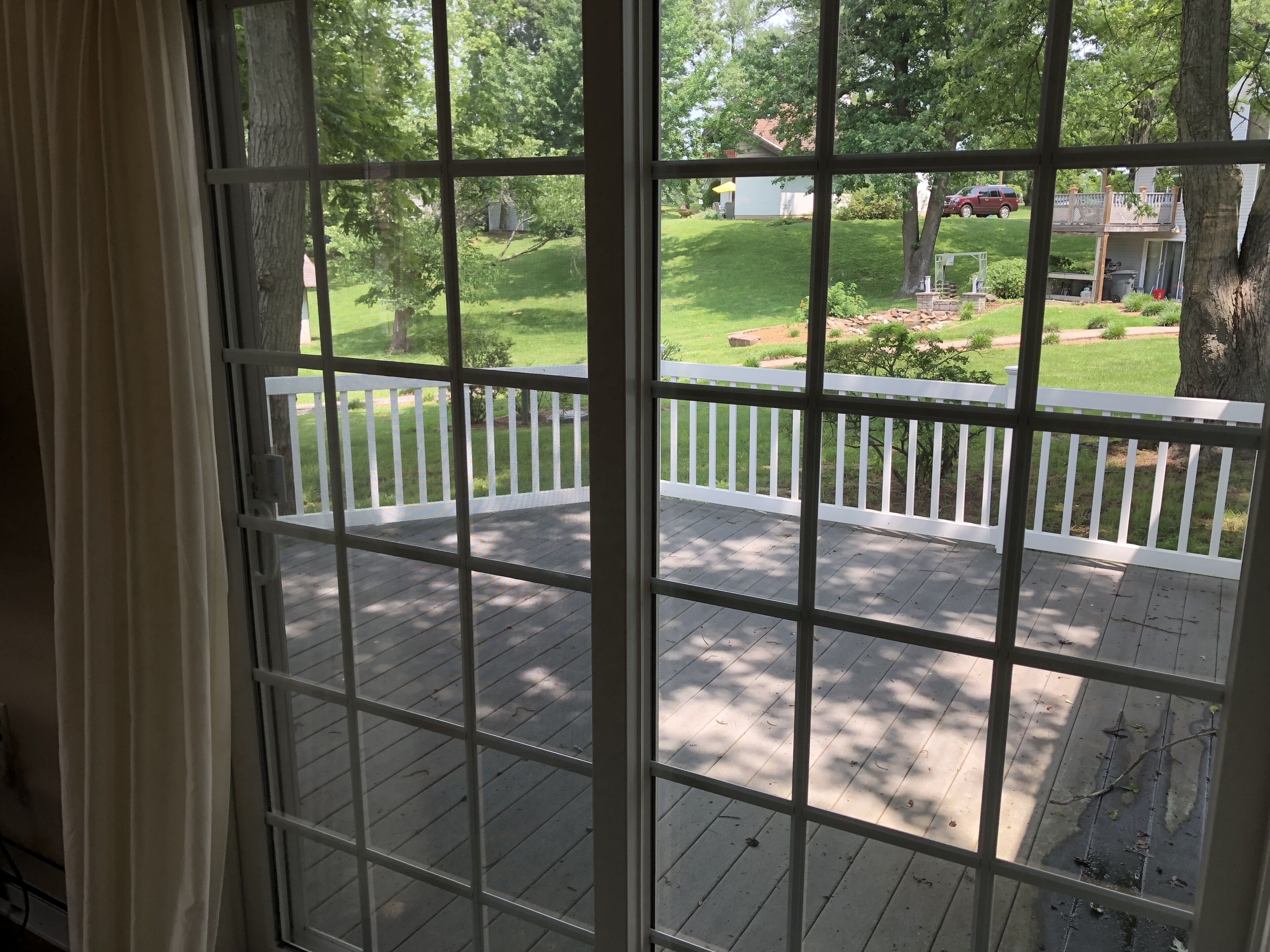 A view through a window with a white railing, looking out onto a wooden deck and a green lawn.