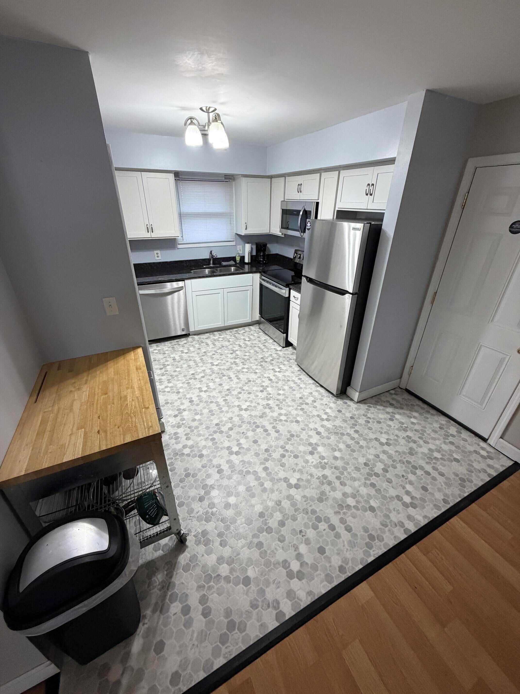 A compact kitchen with white cabinets, a stainless steel refrigerator, a microwave, and a dishwasher.