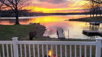 A deck with a fire pit, overlooking a lake with a sunset view.