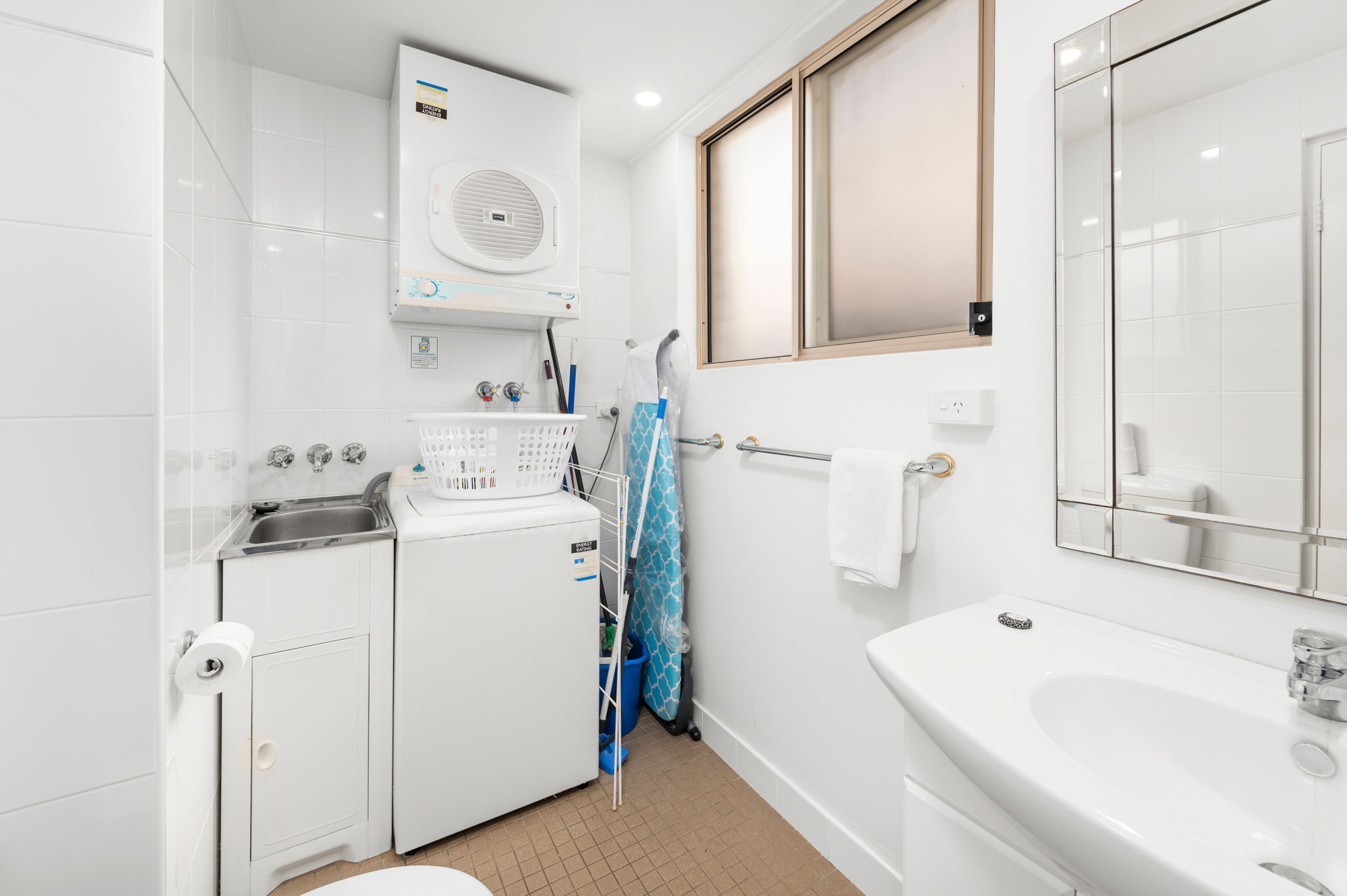 A compact, modern bathroom with a built-in washer and dryer, a large mirror, and a bathtub.