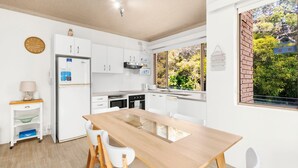Una cocina moderna con armarios blancos, una mesa de comedor de madera y vistas a la vegetación.