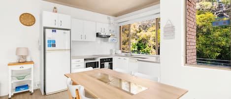 Una cocina moderna con armarios blancos, una mesa de comedor de madera y vistas a zonas verdes.