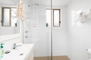 A modern bathroom with a glass shower enclosure, a white sink with a mirror, and a window. - Del Rae 15 Shoal Bay Apartment (Shoal Bay)