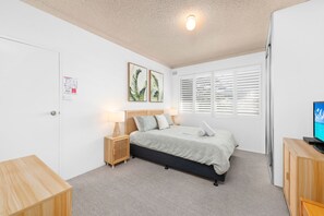 A bedroom with a bed, bedside table, lamp, and a television on a wooden cabinet. - Del Rae 15 Shoal Bay Apartment (Shoal Bay)