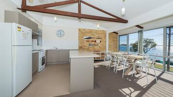 Una cocina moderna con una isla central, electrodomésticos blancos y vistas al mar a través de amplios ventanales.
