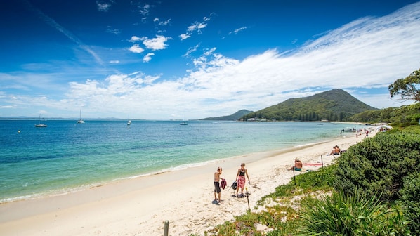 A beach with clear blue water, boats, and a mountainous backdrop. - Castaways 8/17 Shoal Bay Road - The crystal clear waters of Shoal Bay (Shoal Bay)