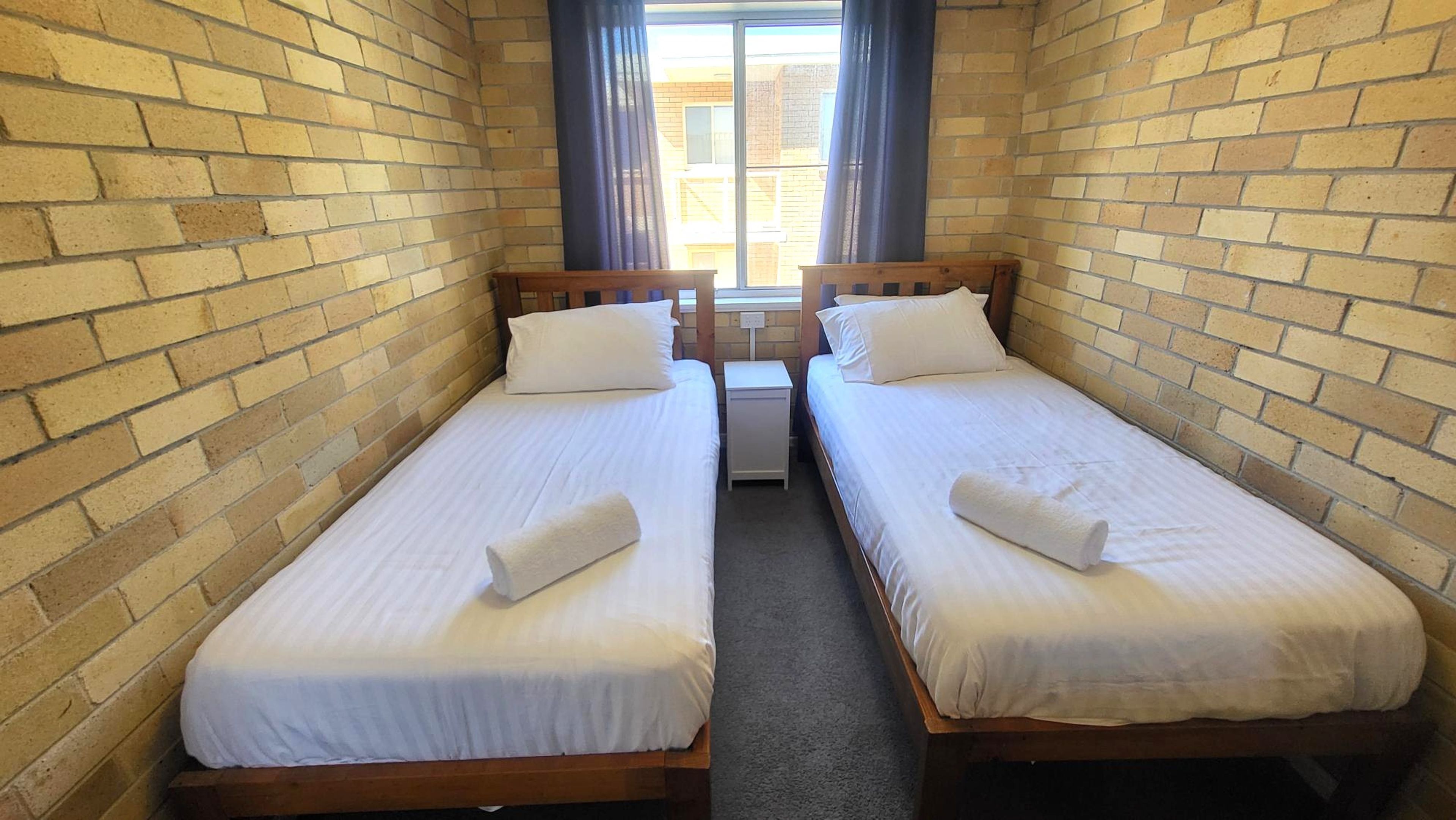 A twin room with two single beds, a small bedside table, and a window with curtains.