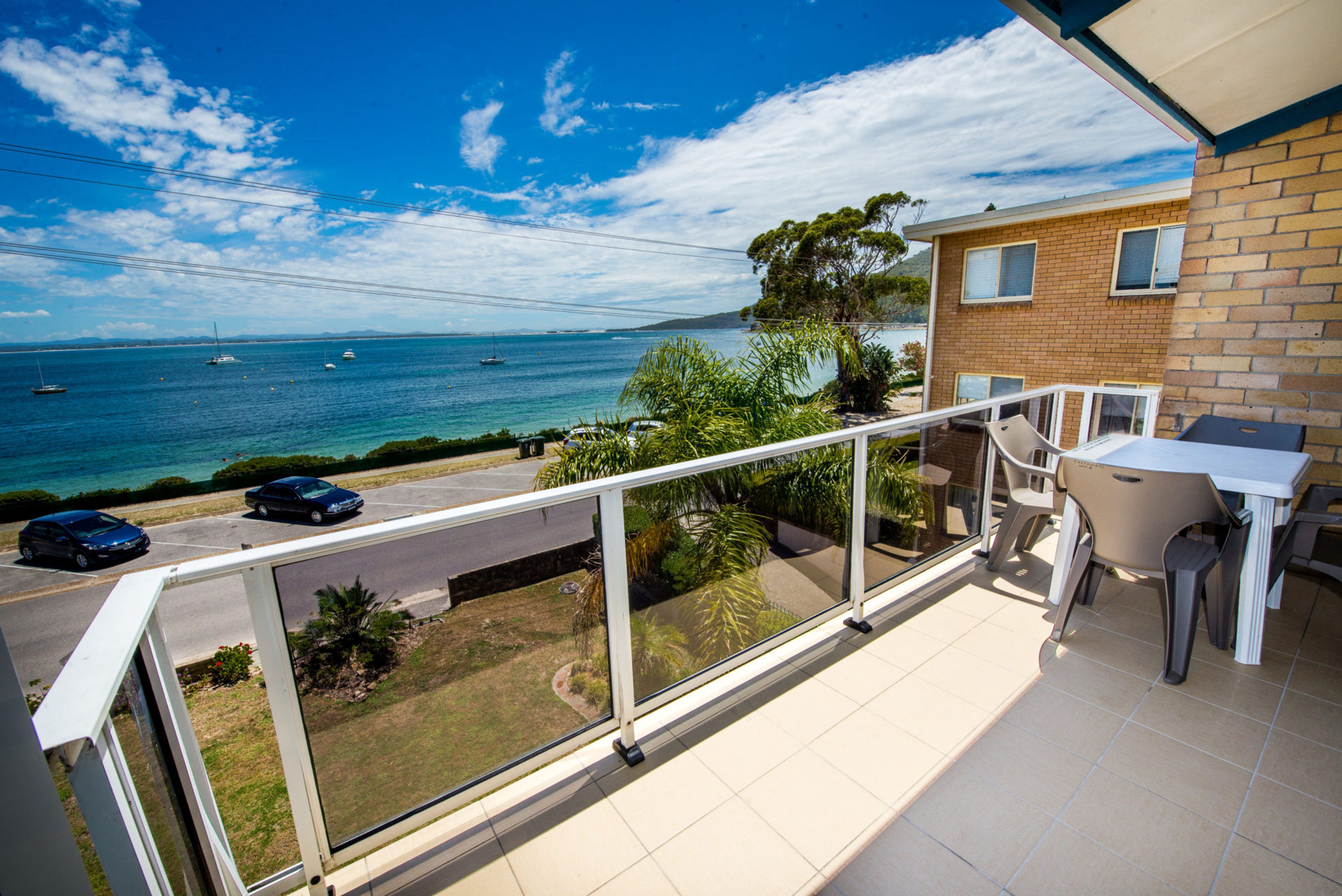 A balcony with a view of the sea, a parked car, and a building with a brick facade.