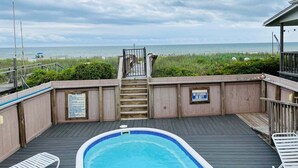 A wooden deck with a pool, a staircase leading to a beach, and a lifeguard sign. - Discover Hidden Treasure: a cozy 2-bedroom oceanfront stay at Holden Beach! (Holden Beach)