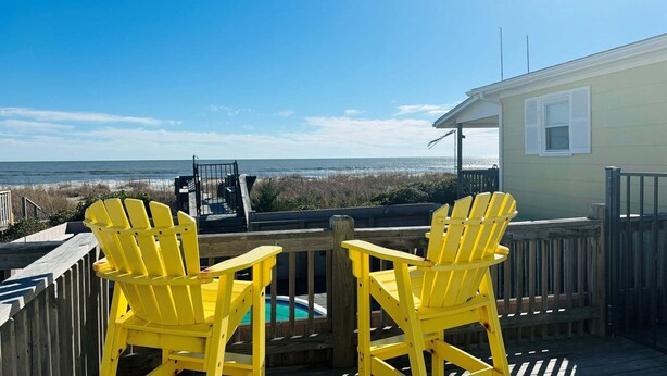 A deck with two yellow Adirondack chairs facing a beach view, a pool, and a small building with shutters. - Discover Hidden Treasure: a cozy 2-bedroom oceanfront stay at Holden Beach! (Holden Beach)