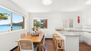 A modern kitchen with white cabinets, a granite countertop, and a view of the sea. - Three bedroom unit in Shoal Bay (Shoal Bay)