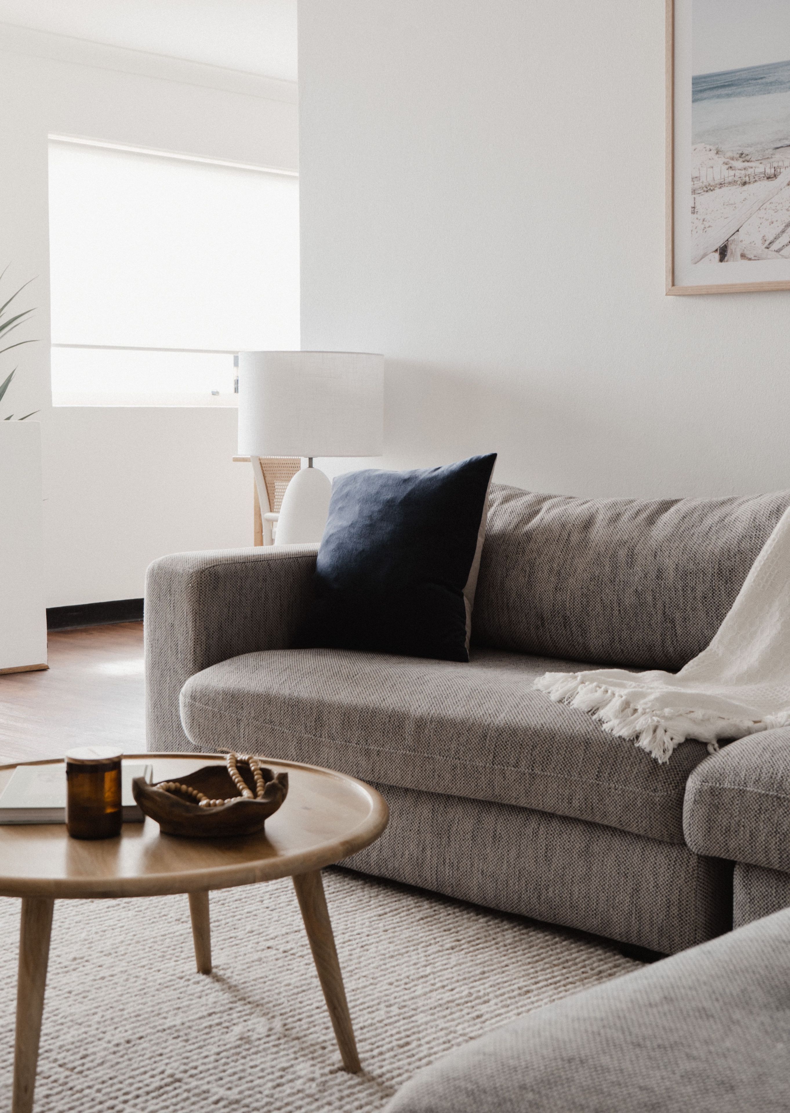 A living room with a grey sofa, a round wooden coffee table, and a lamp.
