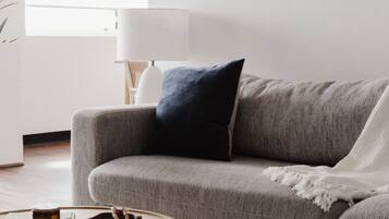 A living room with a grey sofa, a round wooden coffee table, and a lamp.