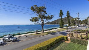 A coastal road with parked cars, a pedestrian path, and a view of the sea with boats. - Three bedroom unit in Shoal Bay (Shoal Bay)