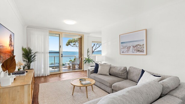 A living room with a sofa, a coffee table, and a view of the sea through large glass doors. - Three bedroom unit in Shoal Bay (Shoal Bay)