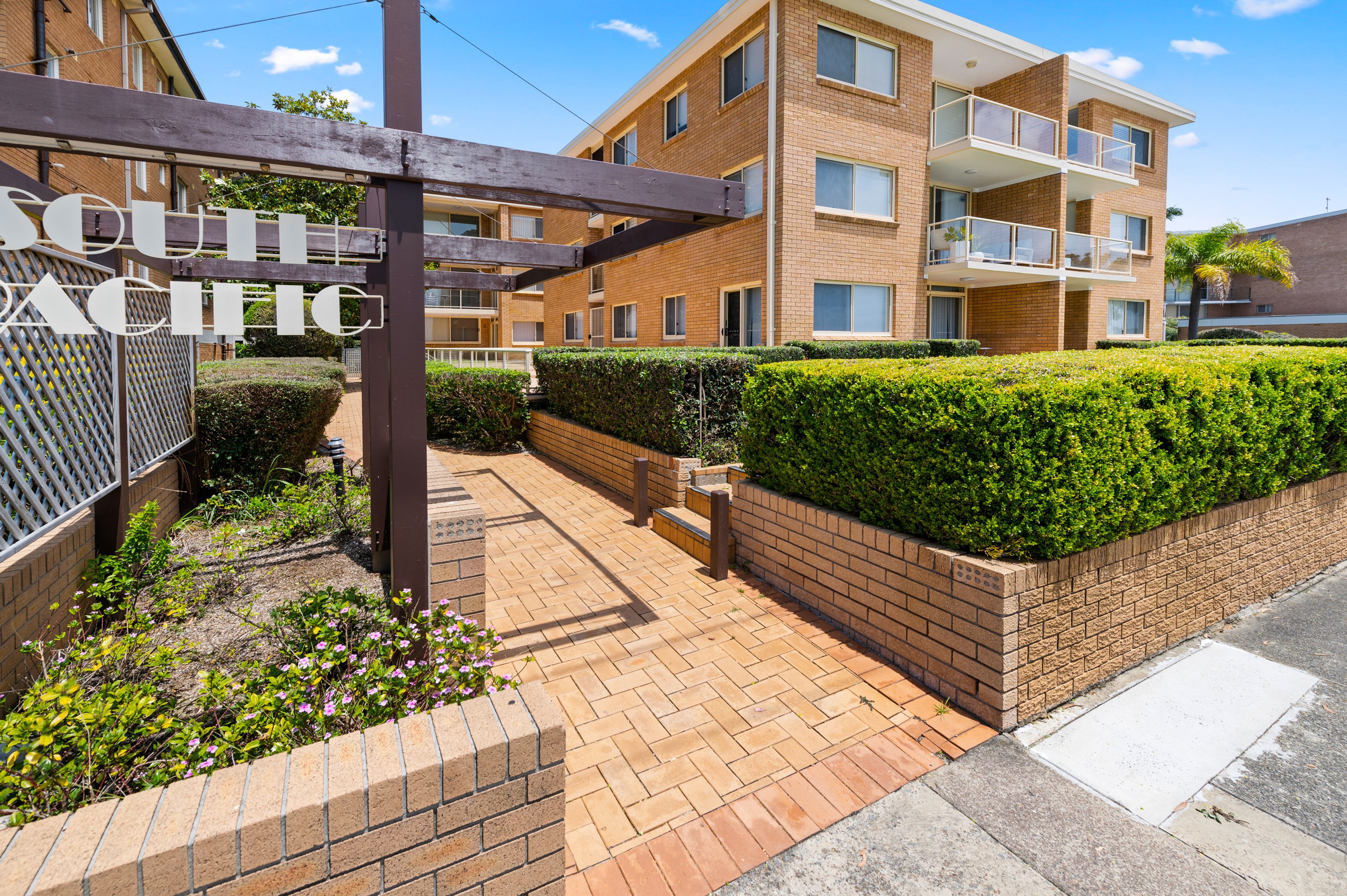 A residential building with a brick facade, balconies, and a well-maintained garden area.