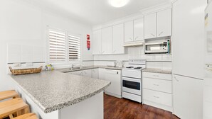 A modern kitchen with white cabinets, a granite countertop, a built-in microwave, and a stove. - Three bedroom unit in Shoal Bay (Shoal Bay)