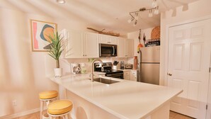 A modern kitchen with white cabinets, a central island with stools, a microwave, a refrigerator, and a sink. - PET FRIENDLY, Private Beach Access, Beach Setup, Pools, HotTub, Tennis/Pickleball, Maravilla 1st Fl (Miramar Beach)
