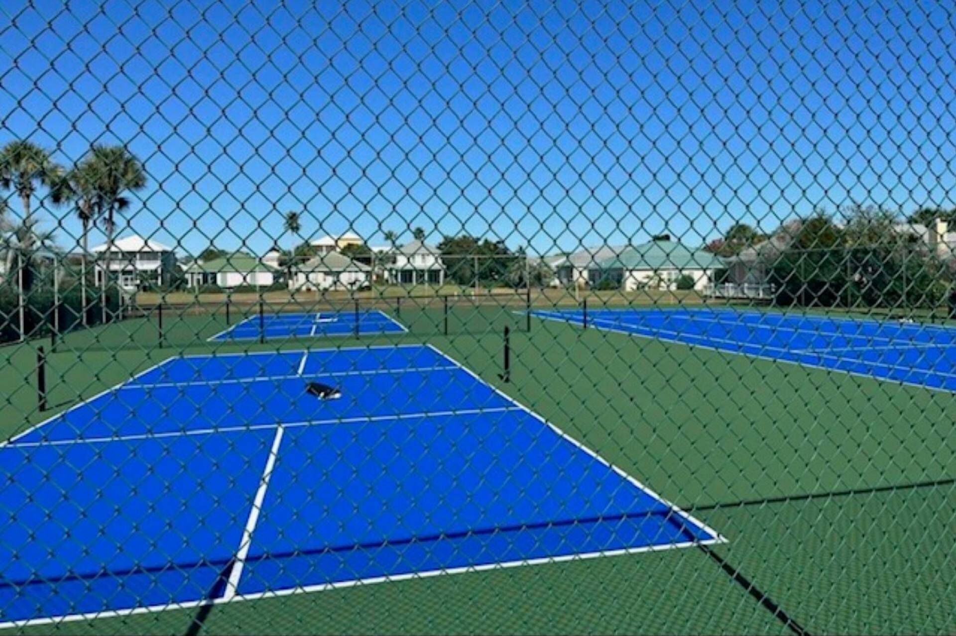 Un campo da tennis circondato da una rete metallica, con cielo sereno.