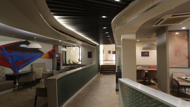 Un hall d’hôtel moderne avec un comptoir d’accueil incurvé, un espace salon et un escalier menant aux étages supérieurs.
