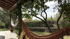 A hammock under a wooden pergola, a potted plant, and a blue bucket on a stone patio.