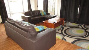 Ein Wohnzimmer mit einem braunen Ledersofa, einem Holztisch und einem gemusterten Teppich.