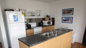 Eine kompakte Küche mit Kühlschrank, Herd, Mikrowelle und Spüle. An der Wand befinden sich Bilder in Rahmen und in der Nähe der Spüle ein Mülleimer.
