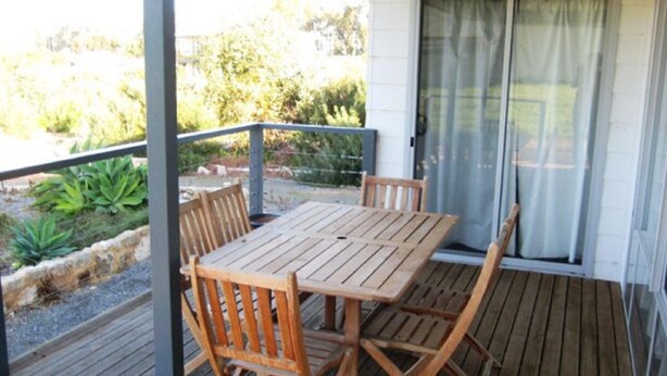 Eine Holzterrasse mit Tisch und Stühlen, eine Glastür und Blick ins Grüne.