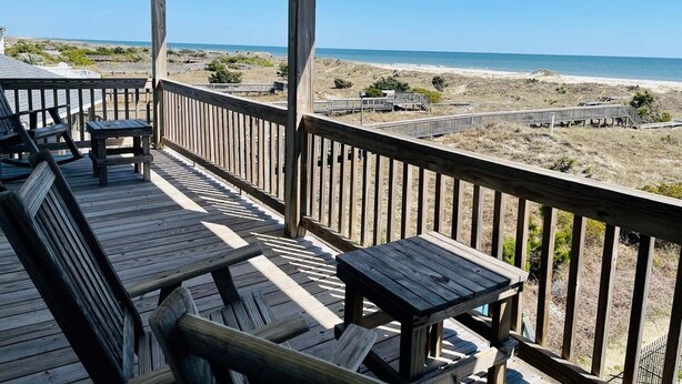Een houten terras met banken en tafels met uitzicht op het strand.