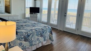 Een slaapkamer met een bed, een televisie, een dressoir en een raam met jaloezieën.