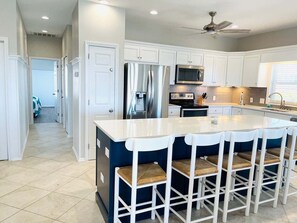 A modern kitchen with white cabinets, stainless steel appliances, a central island with bar stools, and a ceiling fan.