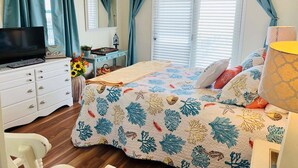 A bedroom with a bed, a TV, a dresser, a desk, and a window with curtains. - Seaside: Spacious 4BR oceanfront home in Holden Beach, perfect for 12 guests. (Holden Beach)