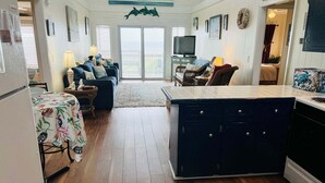 A spacious kitchen with a central island, a dining area with a table and chairs, and a living room with a sofa and a television. - Seaside: Spacious 4BR oceanfront home in Holden Beach, perfect for 12 guests. (Holden Beach)