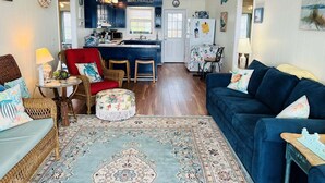 A cozy living room with a blue sofa, a red armchair, and a patterned rug. - Seaside: Spacious 4BR oceanfront home in Holden Beach, perfect for 12 guests. (Holden Beach)
