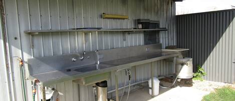A metal outdoor kitchen with a sink, a hose, and a trash can.