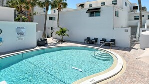 Une piscine avec un panneau indiquant qu’il est interdit de plonger et que la profondeur maximale est de 2,4 mètres. On aperçoit des chaises longues et un palmier à l’arrière-plan.