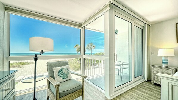 Une chambre avec vue sur la plage, une chaise avec un coussin, une lampe et une petite table.