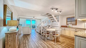 Une cuisine spacieuse avec un plancher en bois, des meubles blancs et un escalier menant à un balcon.