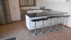 A modern kitchen with a central island, bar stools, stainless steel appliances, and white cabinetry. - Hardwicke Espy   close to beach (Hardwicke Bay)