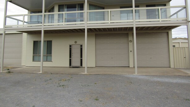 A two-story building with a balcony on the upper floor, a garage on the ground floor, and a door with a window. - Hardwicke Espy   close to beach (Hardwicke Bay)